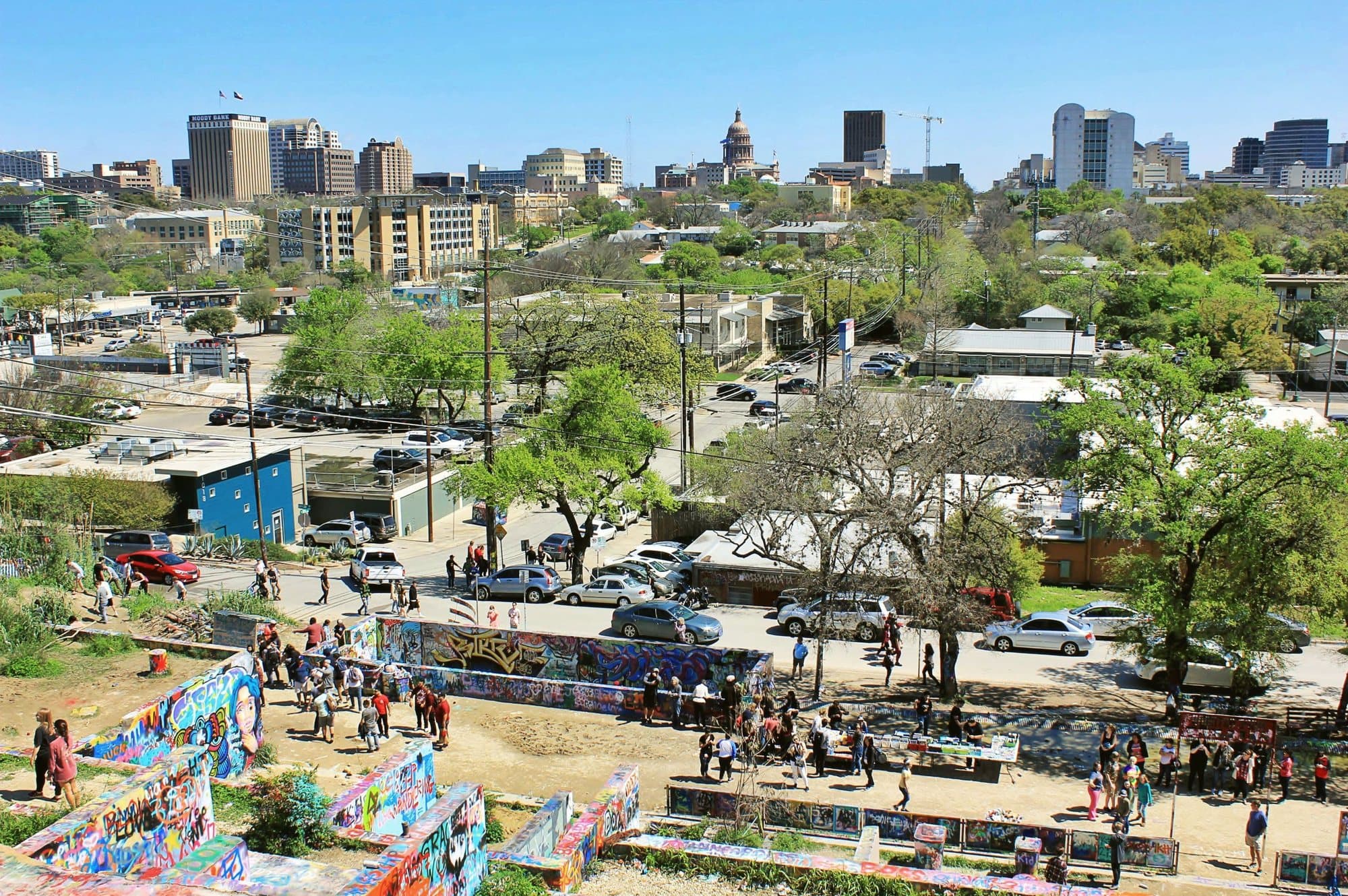 A terraced outdoor graffiti park under a clear sky, with the Austin skyline in the distance.