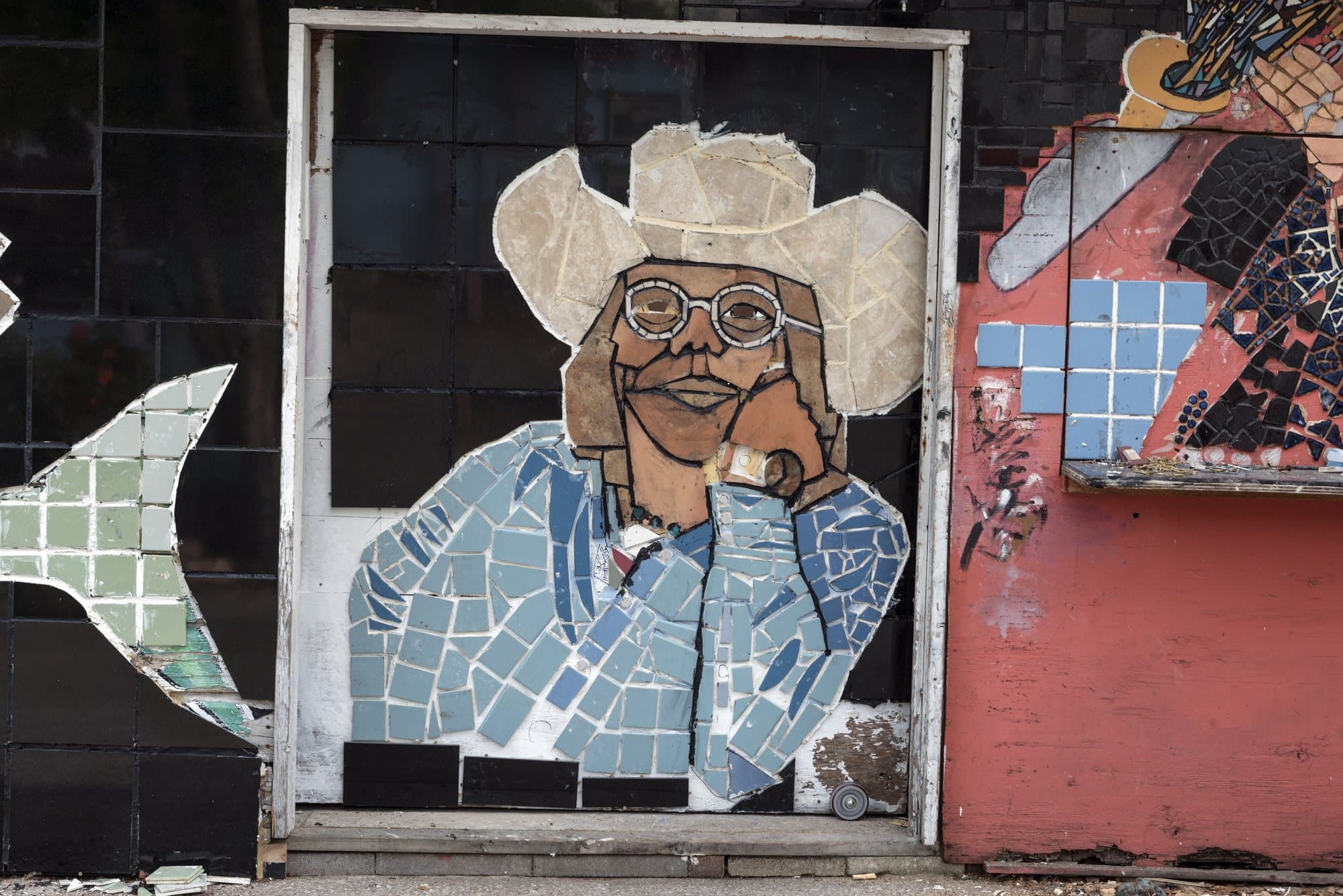 A tiled mosaic portrait of a person in a cowboy hat on a weathered outdoor wall.